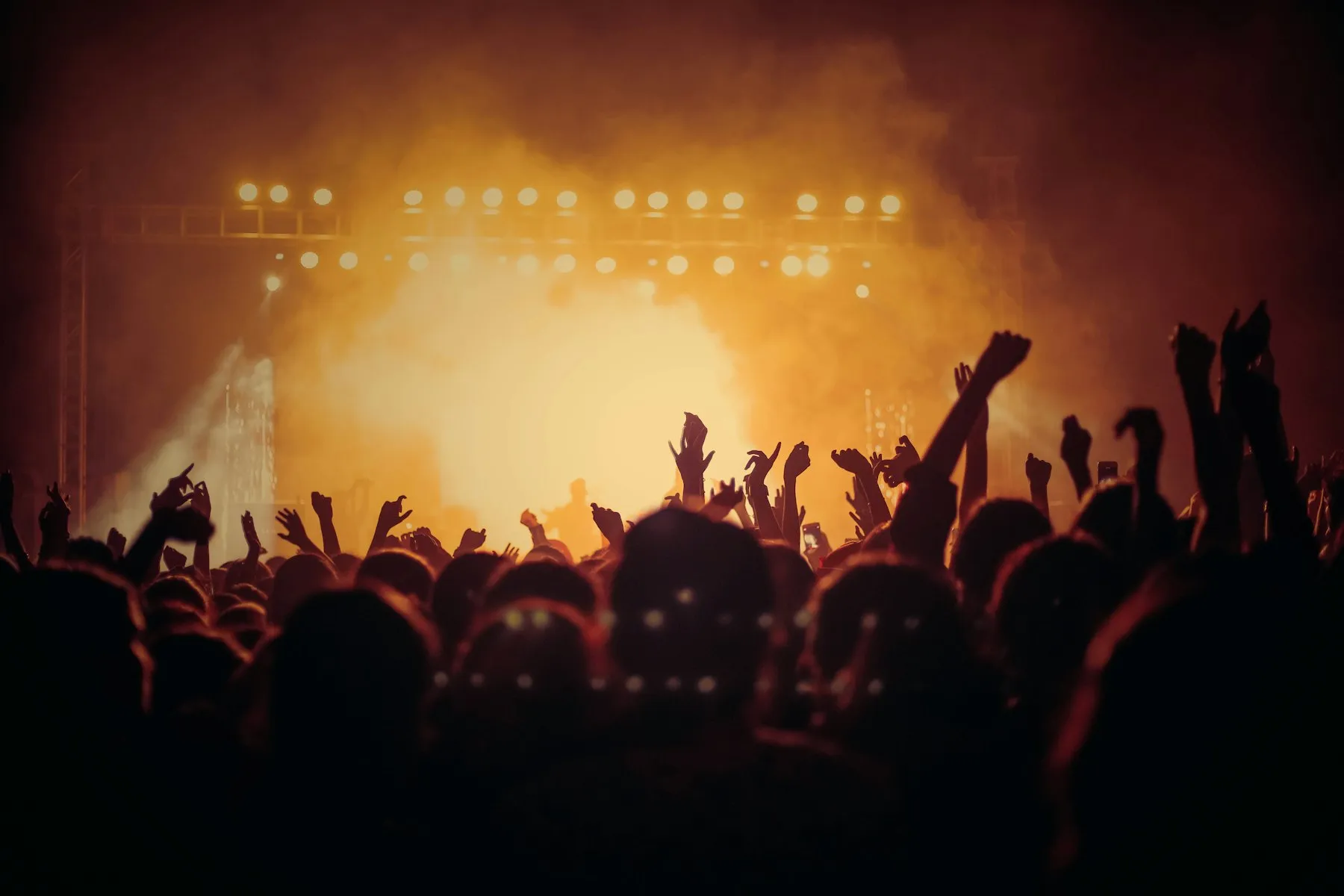 A packed concert crowd with hands raised, silhouetted against orange stage light