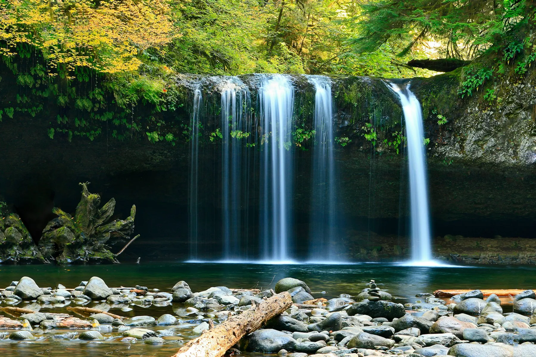 A waterfall pouring from a mossy cliff into a clear mountain pool